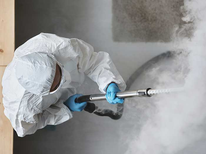 Tatortreiniger in Schutzkleidung entfernt eingetrocknete Blutflecken mit Dampfgerät